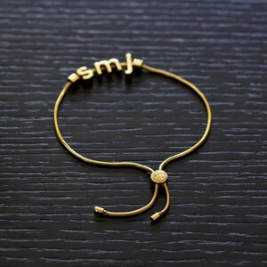 K&ouml;nnte beinhalten: Ein goldenes Kettenarmband mit einem Schiebeverschluss und einem Anh&auml;nger mit den Buchstaben "SMJ".