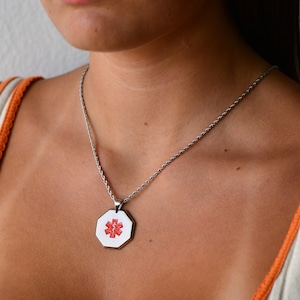 May include: A silver chain necklace with a silver octagonal pendant featuring a red medical symbol.