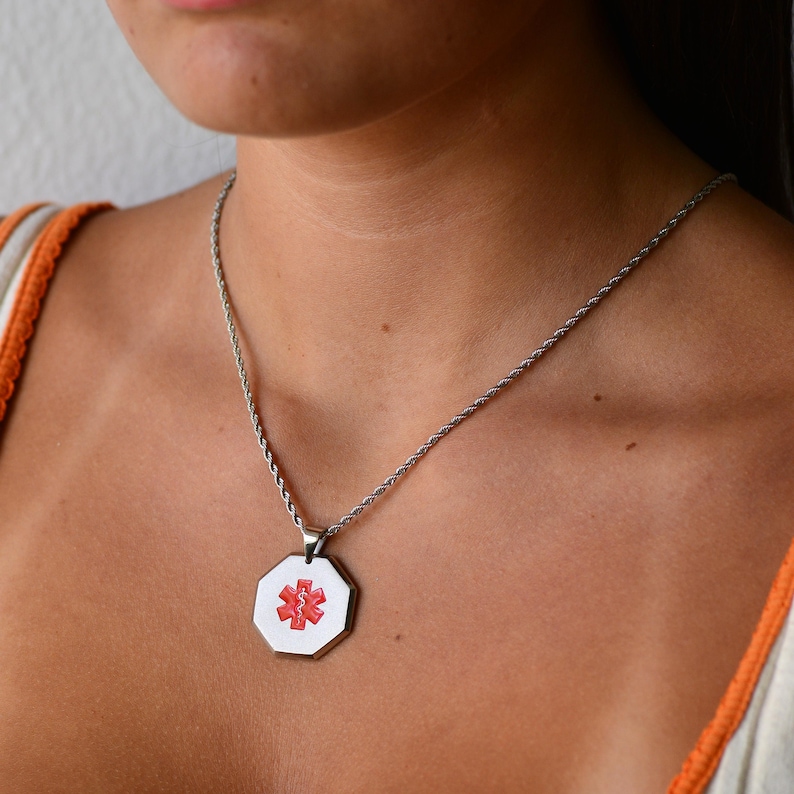 May include: A silver chain necklace with a silver octagonal pendant featuring a red medical symbol.