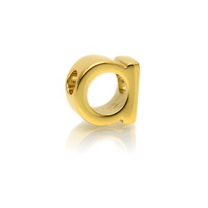 K&ouml;nnte beinhalten: Goldener 'a'-Anh&auml;nger mit einem Loch zum Einf&auml;deln in eine Halskette oder ein Armband.