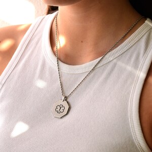 May include: A silver chain necklace with a silver octagonal pendant featuring a medical symbol.
