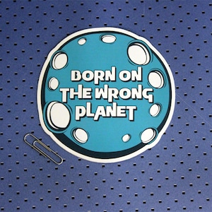 May include: A blue and white sticker with a moon design and the text "Born on the wrong planet".
