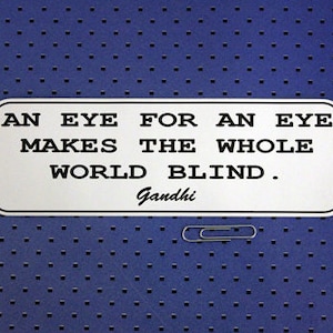 May include: White rectangular sign with black text that reads "An eye for an eye makes the whole world blind."  The text "Gandhi" is written below the quote.