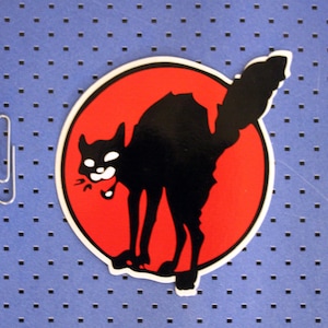May include: A black cat silhouette with a white mouth and eyes, on a red circle background. The cat is facing left and has its tail curled around its body.