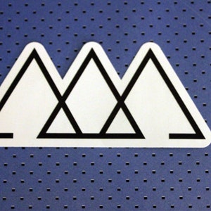 May include: A white sticker with a black outline of three overlapping triangles. The triangles are arranged in a mountain shape.