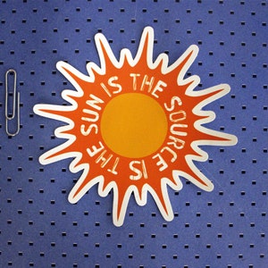 May include: A white sticker with an orange sun in the center. The text around the sun reads "The sun is the source".
