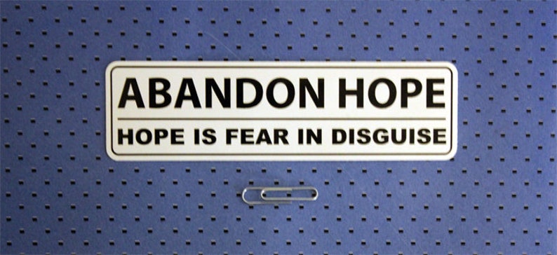 May include: White rectangular sign with black text that reads "Abandon Hope Hope is Fear in Disguise".