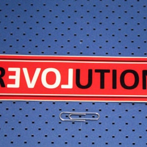 May include: A red rectangular sticker with white and black lettering that reads "REVOLUTION".
