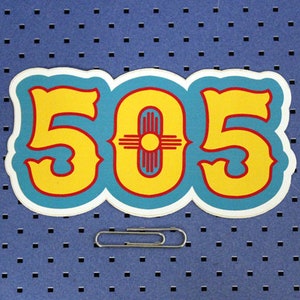 May include: A blue and yellow sticker with the number 505 in a stylized font. The number is surrounded by a red outline. In the center of the sticker is a red and yellow symbol with a sun in the center.