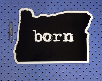 May include: Black and white sticker of the state of Oregon with the word "born" printed in white on a black background.