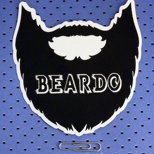 May include: A black and white sticker in the shape of a beard with the word "BEARDO" in white, stylized text. A silver paperclip rests below the sticker on a blue background with small black squares.