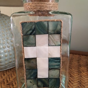 Green tinted triangular glass container with mother of pearl cross motif, jute trim and cork lid
