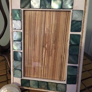 May include: White picture frame with a woven mat and a border of green and white iridescent tiles.