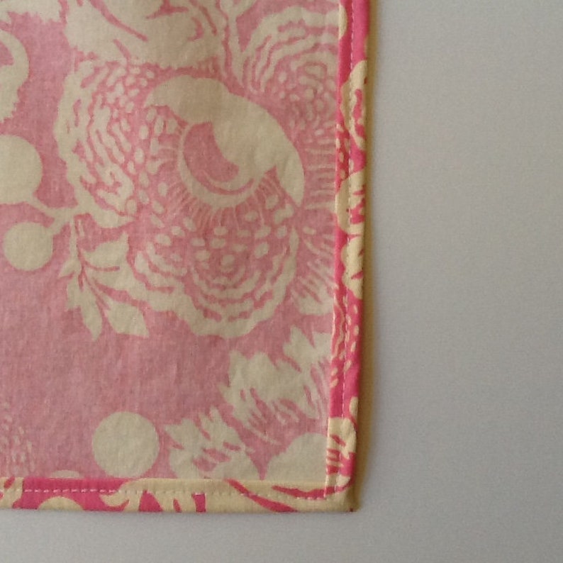 May include: A close-up of a pink and cream floral pattern fabric. The fabric features a large floral design with a pink background and cream-colored flowers. The edges are trimmed with a pink border.