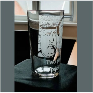 Puede incluir: Un vaso de pinta de vidrio transparente con un dise&ntilde;o grabado de un hombre con bigote y sombrero. El texto "Two pints, please" est&aacute; grabado debajo de la imagen.