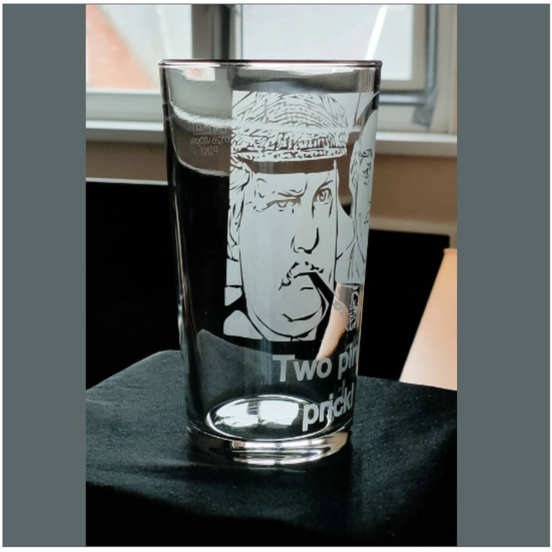 Puede incluir: Un vaso de pinta de vidrio transparente con un dise&ntilde;o grabado de un hombre con bigote y sombrero. El texto "Two pints, please" est&aacute; grabado debajo de la imagen.