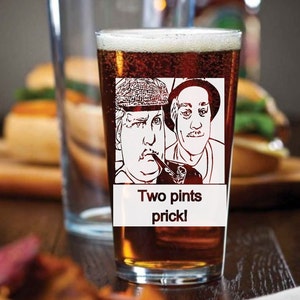 Puede incluir: Un vaso de pinta de vidrio transparente con cerveza marr&oacute;n en su interior. El vaso tiene una imagen en blanco y negro de dos hombres con el texto "Two pints prick!" impreso en la parte delantera.