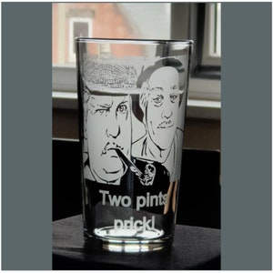Puede incluir: Un vaso de pinta de vidrio transparente con una imagen grabada en blanco y negro de dos hombres. Los hombres llevan sombreros y uno de ellos sostiene una pipa. El texto "Two pints" y "prick!" est&aacute; grabado en el vaso.