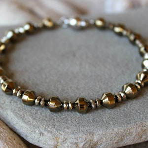 Könnte beinhalten: Ein silbernes und goldenes Armband mit einem Verschluss. Die Perlen sind facettiert und haben eine metallische Oberfläche.