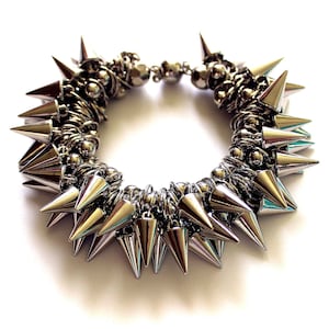 May include: A silver bracelet with a circle of sharp metal spikes. The bracelet is made of metal wire and beads.