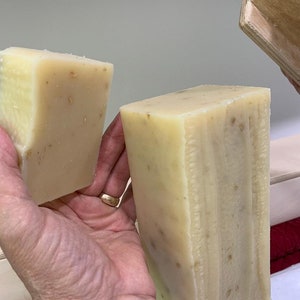 K&ouml;nnte beinhalten: Zwei handgemachte Seifenst&uuml;cke, eines ist ein kleineres St&uuml;ck und das andere ein gr&ouml;&szlig;eres St&uuml;ck. Beide St&uuml;cke sind hellbeige mit braunen Flecken.