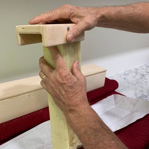 K&ouml;nnte beinhalten: Die H&auml;nde einer Person dr&uuml;cken auf eine h&ouml;lzerne Seifenform. Ein St&uuml;ck hellgr&uuml;ner Seife wird aus der Form gedr&uuml;ckt. Die Seife liegt auf einem wei&szlig;en Blatt Papier.