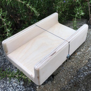 May include: A wooden cheese board with a wire cutter. The board is made of light wood and has a simple design.