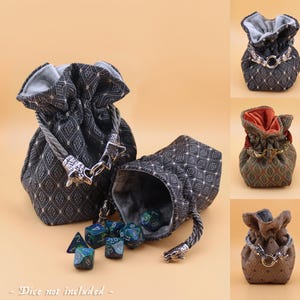 May include: Four different dice bags with a geometric pattern. The bags are made of fabric and have a drawstring closure. Each bag has a metal clasp with a wolf head design. The bags are displayed on a light brown background. "Dice not included" is written at the bottom of the image.