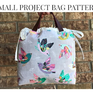 May include: A small project bag with a bird pattern. The bag is light gray with colorful birds in flight. It has brown leather handles and the text "SMALL PROJECT BAG PATTERN" and "NO ZIPPER BEGINNER" in black.