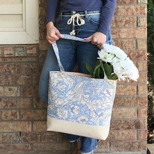 May include: A large tote bag with a blue and white floral pattern. The bag has a cream-coloured bottom and two long handles.