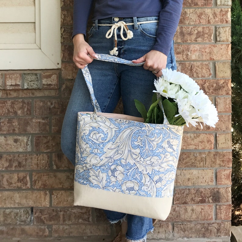 May include: A large tote bag with a blue and white floral pattern. The bag has a cream-coloured bottom and two long handles.