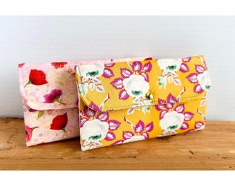 May include: Two fabric wallets with floral patterns. One wallet is pink with red flowers and the other is yellow with pink and white flowers. Both wallets have a button closure.