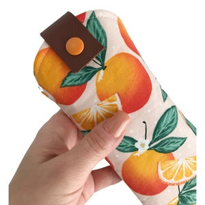 Pode incluir: Uma bolsa de tecido branco com uma al&ccedil;a de couro marrom e um fecho de press&atilde;o. A bolsa &eacute; decorada com um padr&atilde;o de fatias de laranja e folhas verdes.