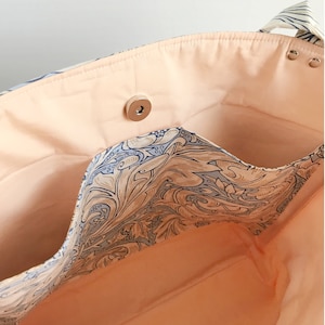 May include: The inside of a tote bag with a peach-coloured lining and a blue and brown floral pattern. The bag has a zipped pocket and a snap closure.