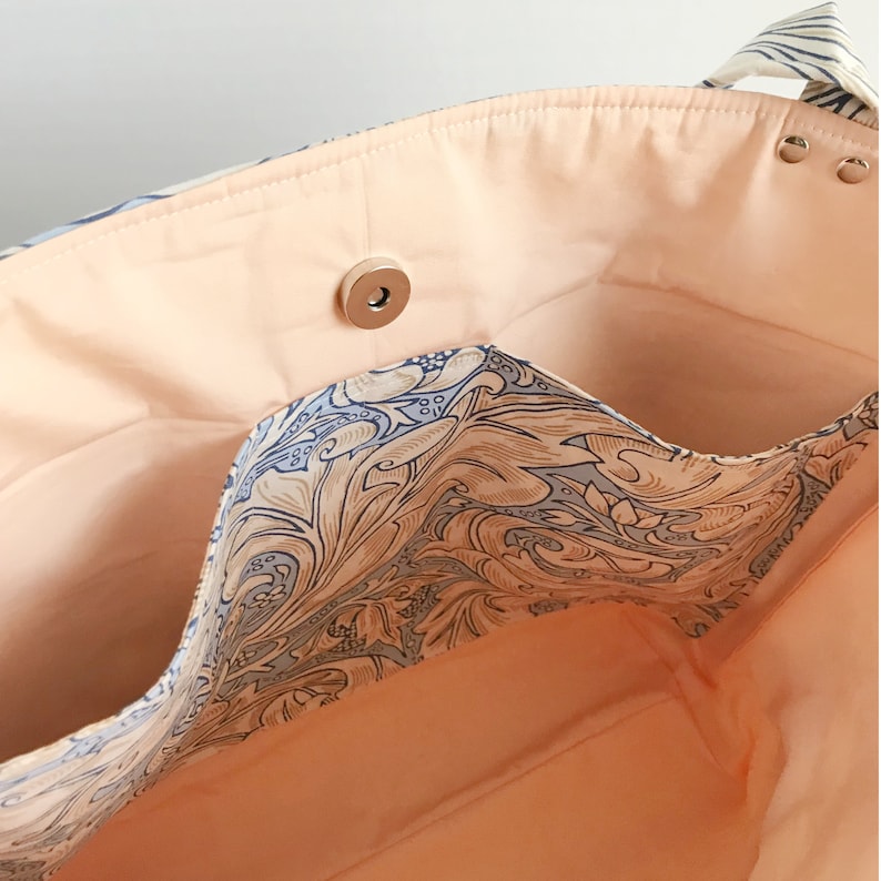 May include: The inside of a tote bag with a peach-coloured lining and a blue and brown floral pattern. The bag has a zipped pocket and a snap closure.
