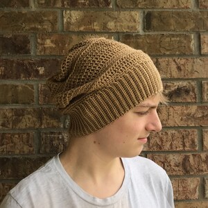 May include: A brown crocheted beanie with a textured pattern. The beanie is worn by a person with light brown hair.