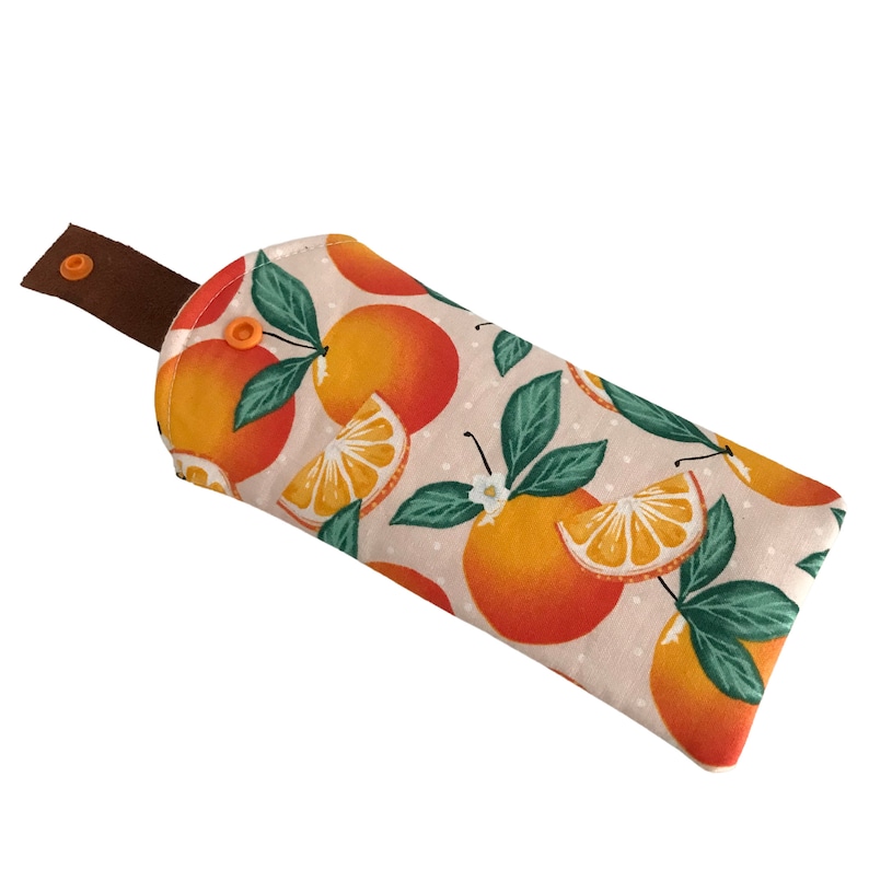 Pode incluir: Uma m&aacute;scara para os olhos de tecido castanho com fundo branco e um padr&atilde;o de fatias de laranja e folhas. A m&aacute;scara para os olhos tem uma tira castanha com fecho de press&atilde;o.