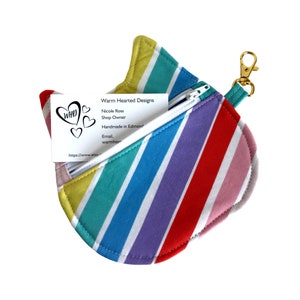 May include: A rainbow striped zippered pouch with a gold keychain. The pouch is open and a business card is visible inside. The business card reads "Warm Hearted Designs, Nicole Ross, Shop Owner, Handmade in Edmonton, Email, warmhearteddesigns@gmail.com, https://www.etsy.com/shop/WarmHeartedDesigns".