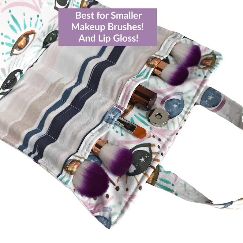 May include: A white makeup brush roll with a colorful eye and star pattern. The roll has multiple pockets for storing makeup brushes and a small lip gloss tube. The text "Best for Smaller Makeup Brushes! And Lip Gloss!" is printed on the roll.