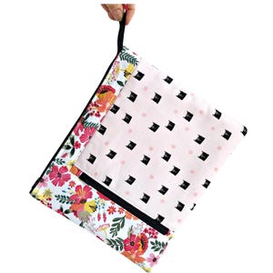 May include: A pink and white zippered pouch with a black cat print on one side and a floral print on the other side. The pouch has a black zipper and a black pull tab.