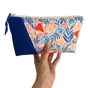 Puede incluir: Una bolsa con cremallera azul y blanca con un estampado floral con mariposas y hojas. La bolsa tiene un panel de tela azul en la parte delantera.