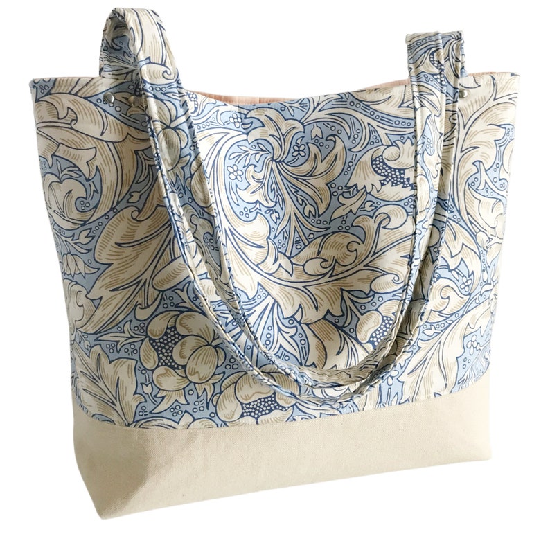 May include: A large tote bag with a blue and beige floral pattern. The bag has two long straps and a beige canvas base.