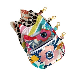 May include: Three colorful fabric zipper pouches with gold keychains. The pouches are in a cat shape and feature different patterns, including floral, leopard print, and stripes.