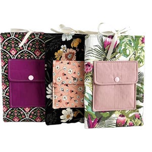 Puede incluir: Tres bolsas de tela con estampados florales y un solo bolsillo en la parte delantera. Las bolsas están forradas con una tela de color sólido y tienen un cierre de botón. Las bolsas están hechas de algodón y son perfectas para guardar objetos pequeños.