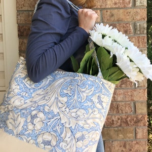 May include: A blue and white floral tote bag with a white canvas base. The bag is filled with a bouquet of white flowers.