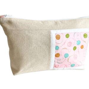 May include: A beige canvas zippered pouch with a pink accent panel featuring colorful yarn balls and the word "meow". The pouch is designed for storing craft supplies or personal items.