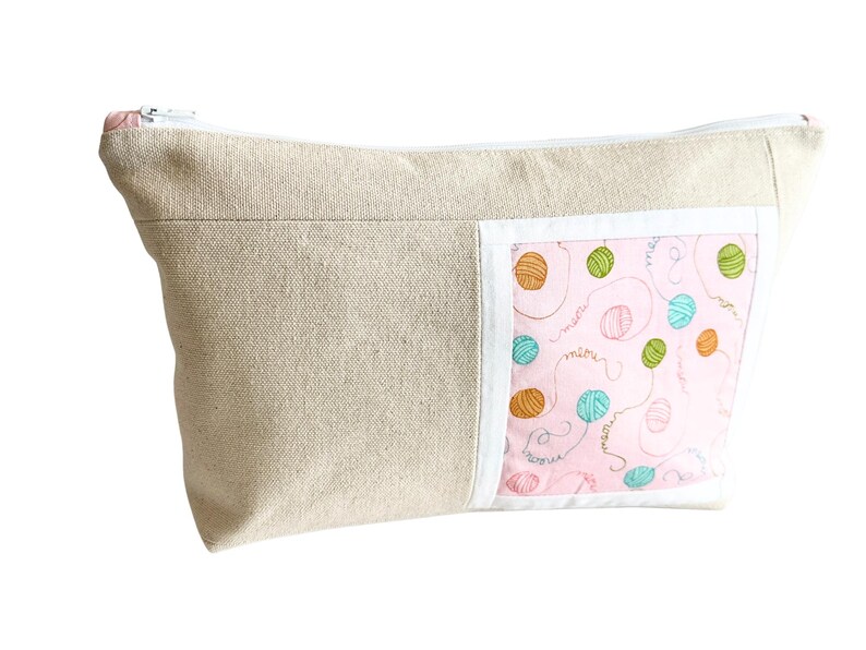 May include: A beige canvas zippered pouch with a pink accent panel featuring colorful yarn balls and the word "meow". The pouch is designed for storing craft supplies or personal items.