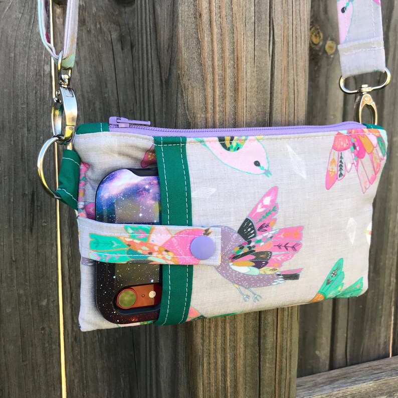 Puede incluir: Una peque&ntilde;a bolsa de tela gris con cierre de cremallera morado y ribete verde. La bolsa tiene un estampado de p&aacute;jaros coloridos y una funda para tel&eacute;fono con estampado de galaxia en el interior.