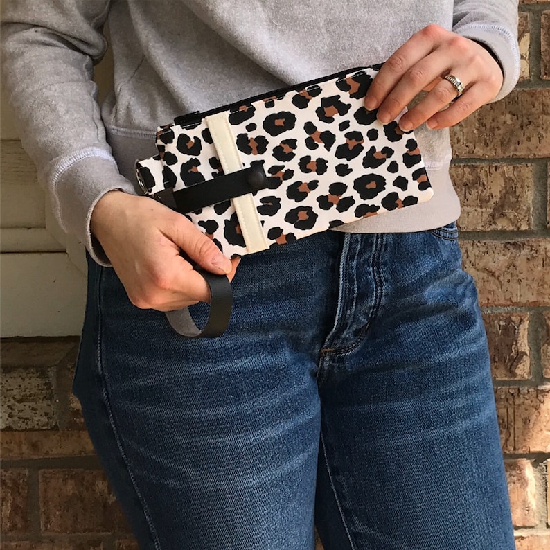 Puede incluir: Una cartera de estampado de leopardo blanco y marr&oacute;n con una correa negra. La cartera la lleva puesta una persona que lleva pantalones vaqueros azules.
