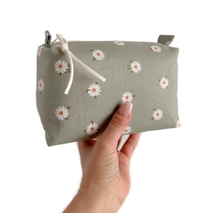 May include: A green fabric makeup bag with a white daisy print and a white drawstring closure.